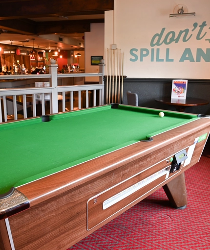 Interior seating area of a pub with a pool table and a bar.