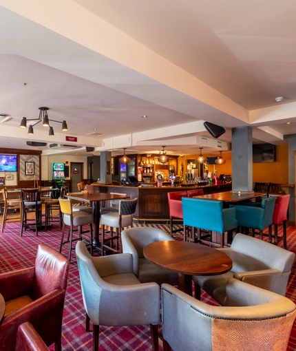 Interior dining area of a pub with a bar, a dartboard, a TV and a pool table.