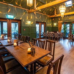 An image showing the interior restaurant seating area with wooden beam vaulted ceiling, tables set out with a floral arrangements and candles at The Black Swan.