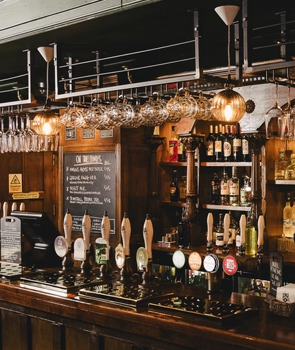 The wood panelled bar inside the Masons Arms, with glasses hanging in racks above the counter, and grape vines carved into the coving above.
