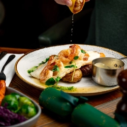 A plated Grilled Halibut dish on a festive decorated wooden table.  A hand is squeezing half a lemon over the fish.
