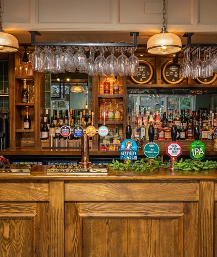 A close up view of the wood panelled bar inside The White Lion in Frenchay, with wine glasses hanging in racks above the counter.