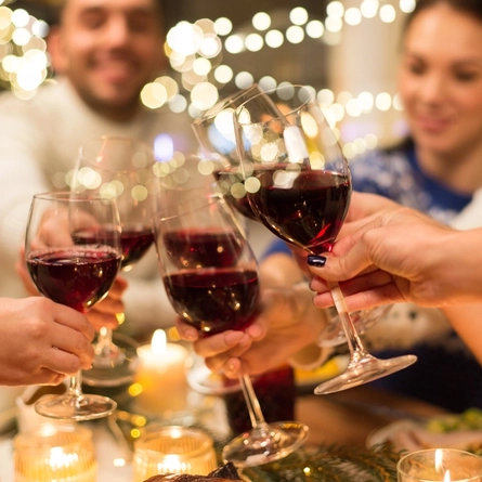 Some glasses of red wine being cheersed at a table.