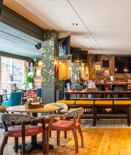 The bar and interior restaurant seating area of The Merlin, with wooden tables and bench seating, TVs on the walls, and pub game machines.