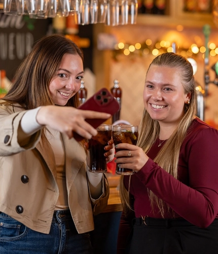 Two women holding a glass of Coca Cola and taking a selfie with a phone