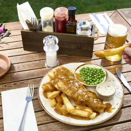A lifestyle image showing a person sat at a table within the exterior beer garden seating area enjoying a main dish and drinks at a Chef & Brewer venue.