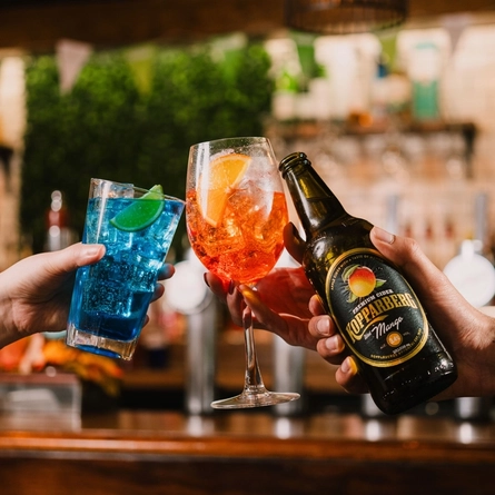 A group of drinks including a bottle of Kopparberg being held up into a 'cheers' position at a Flaming Grill venue.
