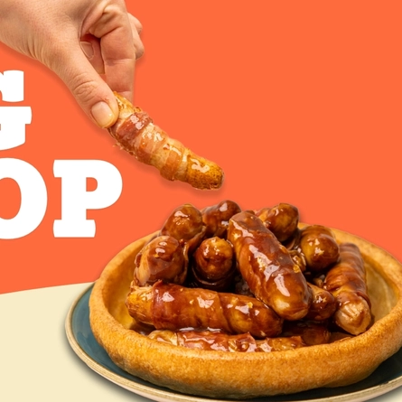 A banner featuring the words "Pig Stop" next to an image of pigs in blankets served in a large Yorkshire pudding, with a hand picking up one of the sausages.