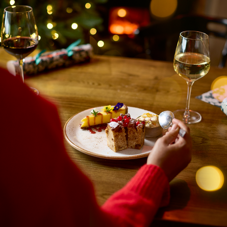 An image of a 3 desserts on a plate and 2 glasses of wine sat on an interior restaurant seating area table at a Chef & Brewer venue.