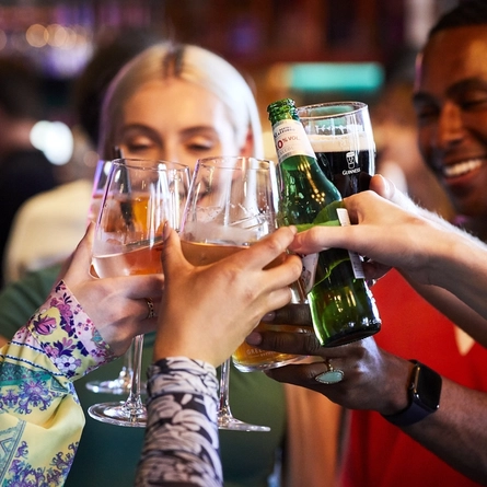 A close up view of a group of people inside a pub bar area, clinking their drinks together.