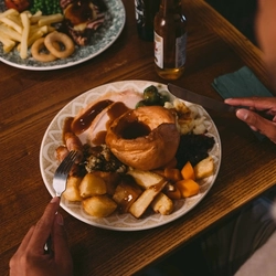 The hands of a person holding cutlery above a plated meal on a festive decorated wooden table.