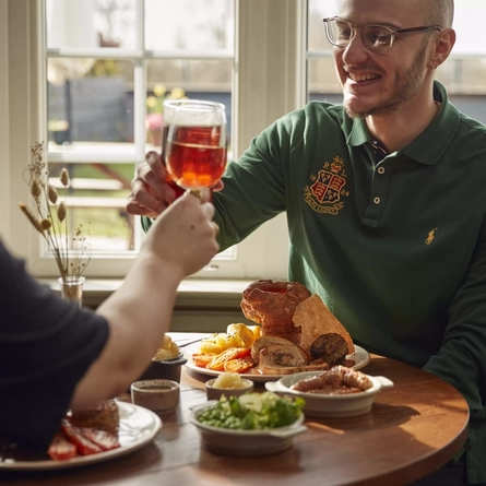 A man cheersing his pint of beer over a roast dinner.