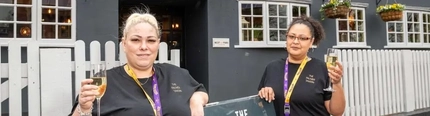 Two women holding glasses of champagne outside of a pub.