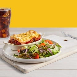 A plate of food next to a glass of coke on a wooden table
