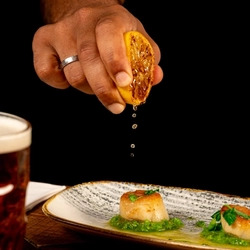 A plated starter of Scallops on a festive decorated wooden table.  A hand is squeezing half a lemon over the scallops.