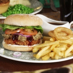 An advertising image focusing on a Festive Chicken Burger dish with various plated Festive Main dishes in the background and a selection of drinks available at a Pub & Carvery venue.