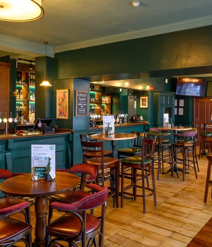 The ground floor bar and interior restaurant seating area at The Globe; with checkerboard tiles in front of the counter, TVs on the walls, two gaming machines, and bar stool seating.