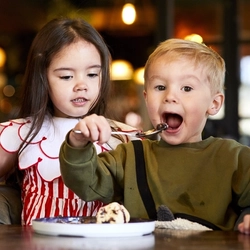 Two children seated at an indoor table, enjoying ice cream.