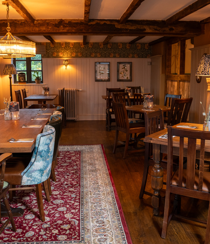 The interior restaurant seating area of Ye Olde Swan in Woughton-On-The-Green, with wooden beams on the ceiling and framed artwork on the walls.