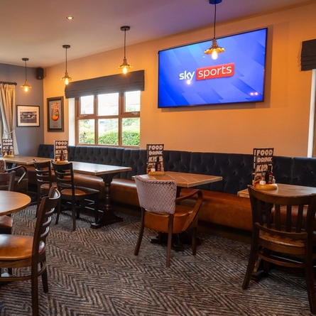An interior restaurant seating area at The Wall's End, with a long, upholstered booth seat below the windows, and a TV on the wall above it.