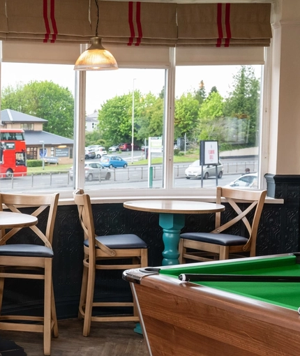 The interior games area at The Tamar, with a dartboard, a pool table, and tables and chairs next to the windows.