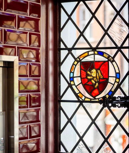 A close up view of the diamond patterned leaded windows of The Golden Lion, with a stained glass golden lion on a red shield.