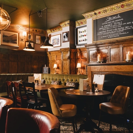The wood panelled interior restaurant seating area at the Masons Arms in Mayfair, with a fireplace, an upholstered booth corner seat, and flowers carved into the coving.