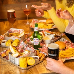 An image focusing on several mains and sharer dishes sat on a table with a selection of drinks at a Flaming Grill venue.