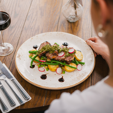 An image of a plated Lamb Rump main dish with a glass of red wine available at Chef & Brewer venues.