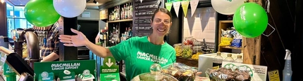 An image of various cakes and pin badges set up on an interior bar to raise money for Macmillan at a Greene King venue.