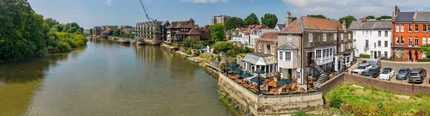 An aerial view of the exterior facade and beer garden seating area of The London Apprentice; the River Thames which runs alongside the pub; and the other buildings situated on the bank of the river.