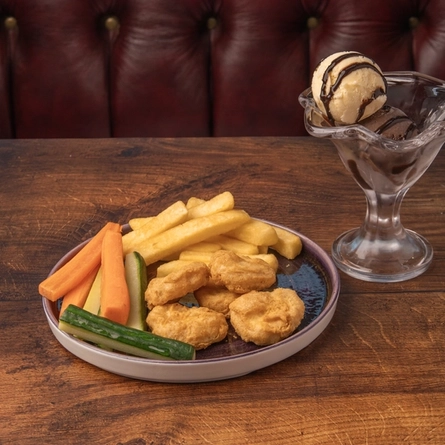 A plated children's serving of chicken nuggets, chips and vegetable crudites next to a portion of ice cream in a sundae dish, on a table.