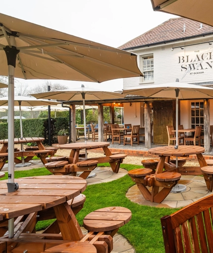 An image showing the exterior beer garden seating area with wooden tables complete with umbrella shades and chairs at The Black Swan.