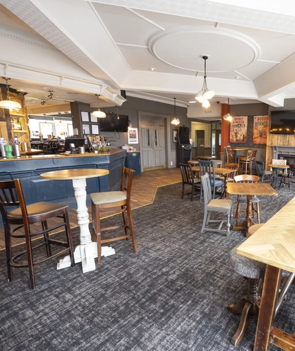 Interior dining area of a pub with a bar, a TV and a fireplace.