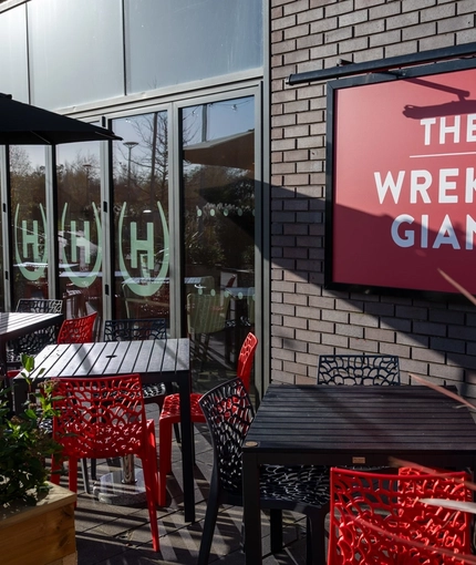 The exterior beer garden seating area at The Wrekin Giant in Telford, with a shade umbrella on one of the tables, and plants in wooden planter boxes.