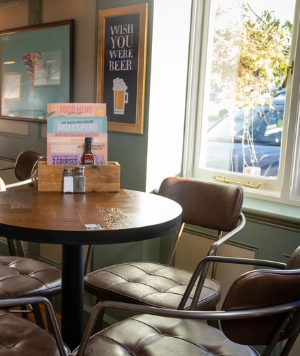 An interior restaurant seating area at the Green Posts, with framed artwork on the wall, and upholstered seats.