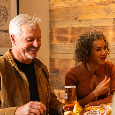 An image showing a group of people sat around a table enjoying mains and sharer dishes with various drinks at a Flaming Grill venue.