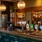A close up view of the bar and beer taps inside The Hollybush in Lichfield, with golden drinks trays on the counter, and three spherical glass lights hanging above.