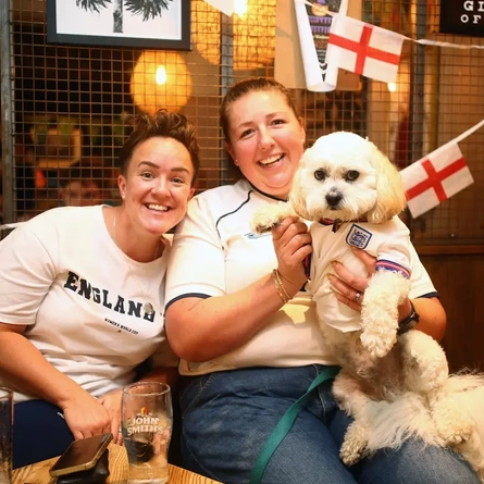 Two women and a dog, all wearing England shirts