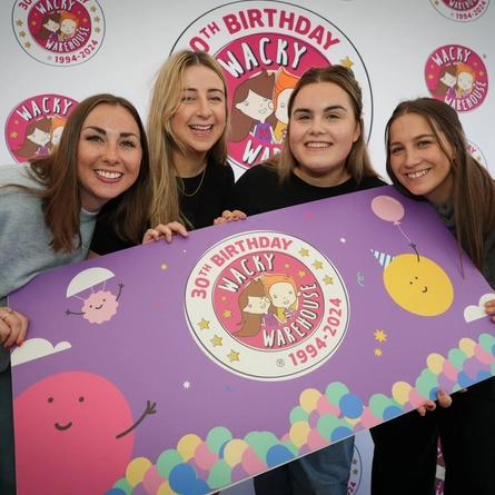 a group of women smiling for the camera holding a Wacky Warehouse poster