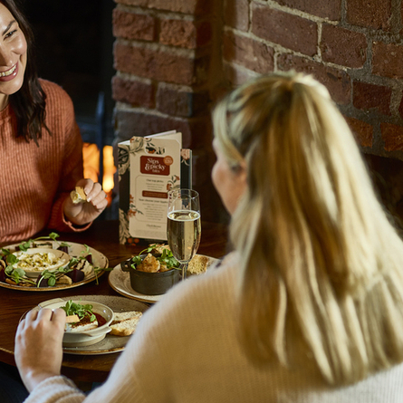 An image of 2 customers sat within the interior restaurant and seating area enjoying a selection of picky bits and drinks available at Chef & Brewer venues.