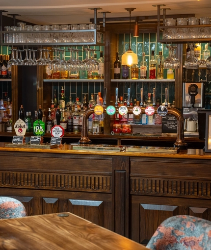 A close up view of the wood panelled bar at The Ship in Bedford; with golden drinks trays on the counter, and glasses hanging in racks overhead.