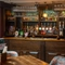 A close up view of the wood panelled bar at The Ship in Bedford; with golden drinks trays on the counter, and glasses hanging in racks overhead.