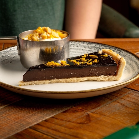 A plated slice of Chocolate Orange tart with a mini pan of ice cream is on a wooden table.