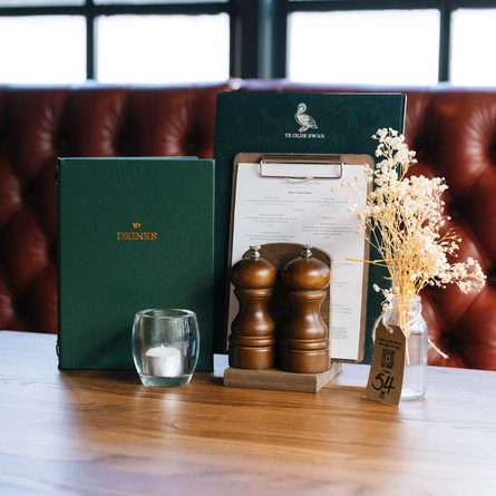 A close up view of menus, salt and pepper mills, a tea light, and a table ornament, on a restaurant table inside Ye Olde Swan.