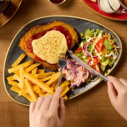 An overhead shot of a plated meal with a pair of hands holding a knife and fork over the plate.