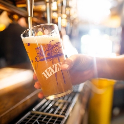 A close up image of a pint of Hazy Day being poured behind the interior bar at a Community Pubs With Food venue.
