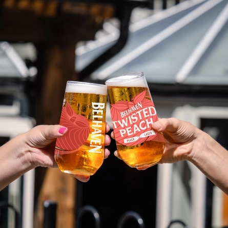 A close up image showing 2 people holding pints of Belhaven Twisted Peach and celebrating with a cheers.