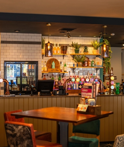 The bar and interior restaurant seating area of The Merlin in Edinburgh, with wooden tables and upholstered seats.