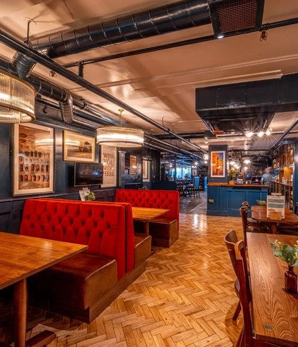 The interior restaurant seating area of the Monument, with wooden tables and chairs, booth seating, and TVs on the wall.